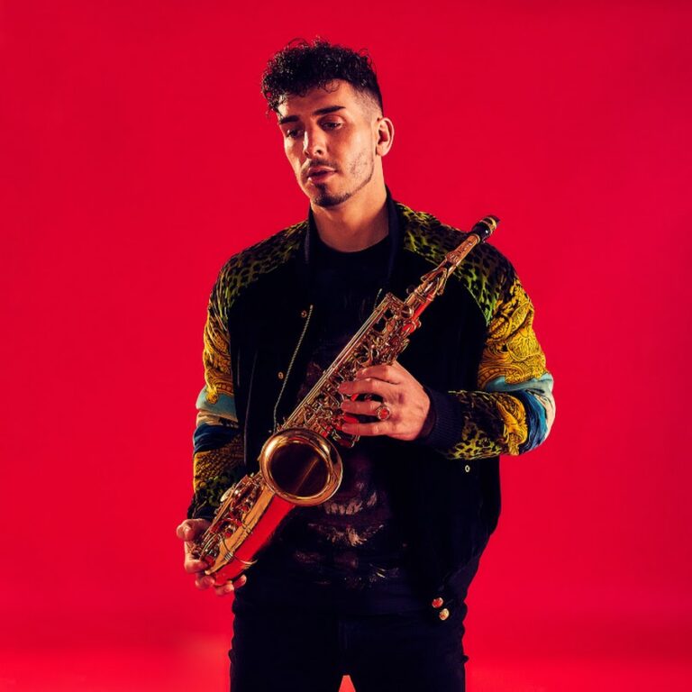 picture of John on sax holding saxophone with red background